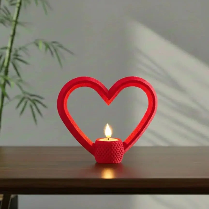 A bright red, hollow heart-shaped frame holding a glowing tealight candle at its base. The sculpture sits on a wooden table with sunlight shadows in the background.