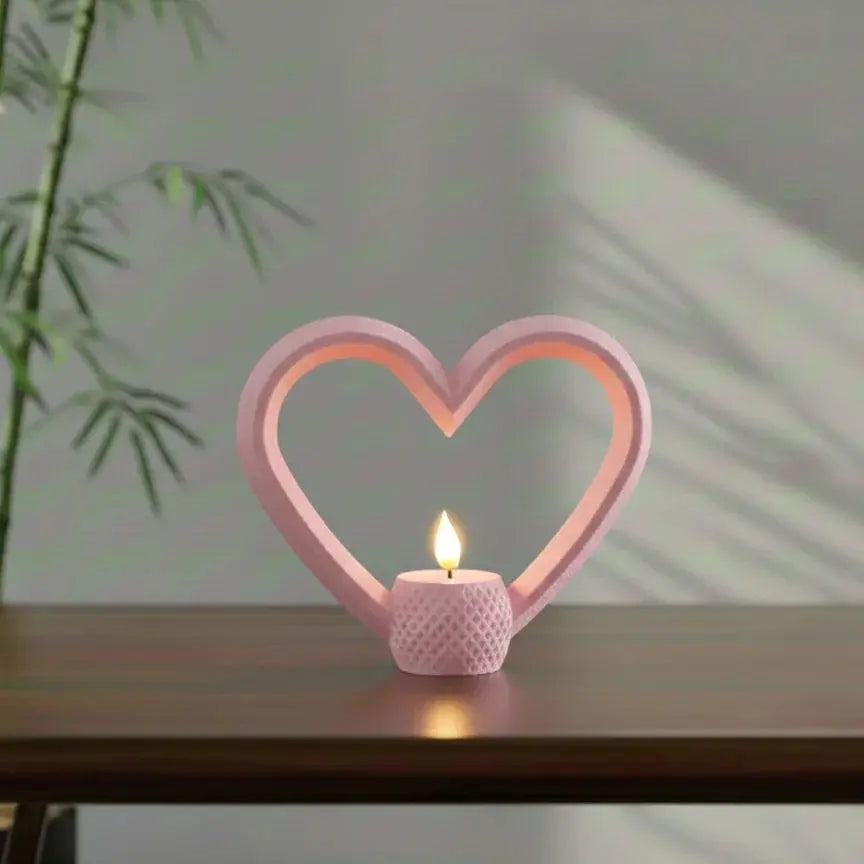 A bright red, hollow heart-shaped frame holding a glowing tealight candle at its base. The sculpture sits on a wooden table with sunlight shadows in the background.