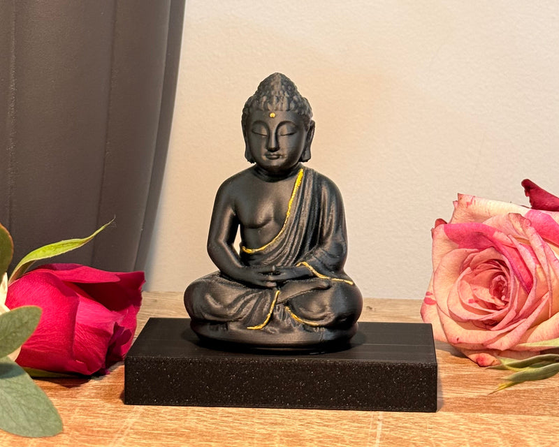 Small Buddha statue on a wooden surface with pink flowers and green leaves in the background